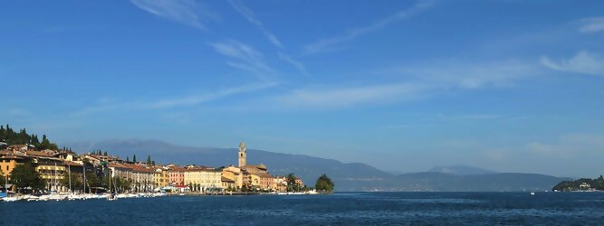 Trip Lanzarote beliebte Urlaubsziele am Gardasee -  Mit einer Fläche von 370 km² ist der Gardasee der größte See Italiens. Es liegt am Fuße der Alpen und erstreckt sich über drei Staaten: Lombardei, Venetien und Trentino. Die maximale Tiefe des Sees beträgt 346 m, er hat eine längliche Form und sein nördliches Ende ist sehr schmal. Dort ist der See von den Bergen der Gruppo di Baldo umgeben. Du trittst aus deinem gemütlichen Hotelzimmer und es begrüßt dich die warme italienische Sonne. Du blickst auf den atemberaubenden Gardasee, der in zahlreichen Blautönen schimmert - von tiefem Dunkelblau bis zu funkelndem Türkis. Majestätische Berge umgeben dich, während die Brise sanft deine Haut streichelt und der Duft von blühenden Zitronenbäumen deine Nase kitzelt. Du schlenderst die malerischen, engen Gassen entlang, vorbei an farbenfrohen, blumengeschmückten Häusern. Vereinzelt unterbricht das fröhliche Lachen der Einheimischen die friedvolle Stille. Du fühlst dich wie in einem Traum, der nicht enden will. Jeder Schritt führt dich zu neuen Entdeckungen und Abenteuern. Du probierst die köstliche italienische Küche mit ihren frischen Zutaten und verführerischen Aromen. Die Sonne geht langsam unter und taucht den Himmel in ein leuchtendes Orange-rot - ein spektakulärer Anblick.